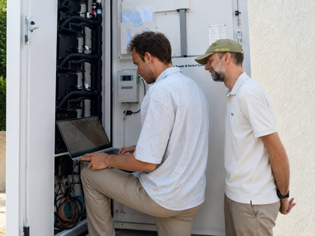 Two men are looking at data on a computer inside a container that holds batteries.